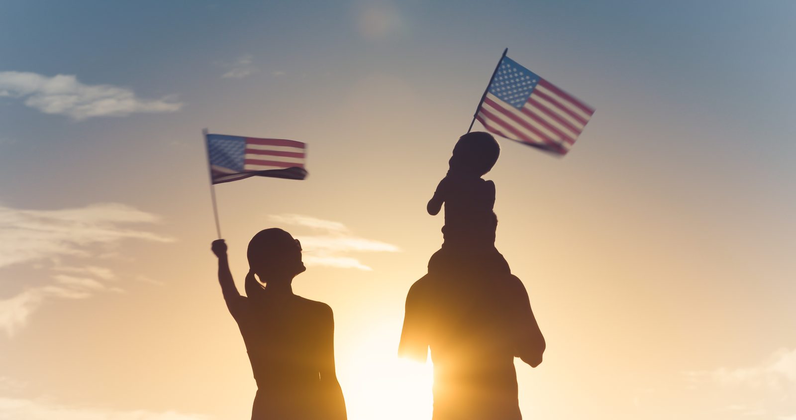 Family silhouettes waving American flags at sunset