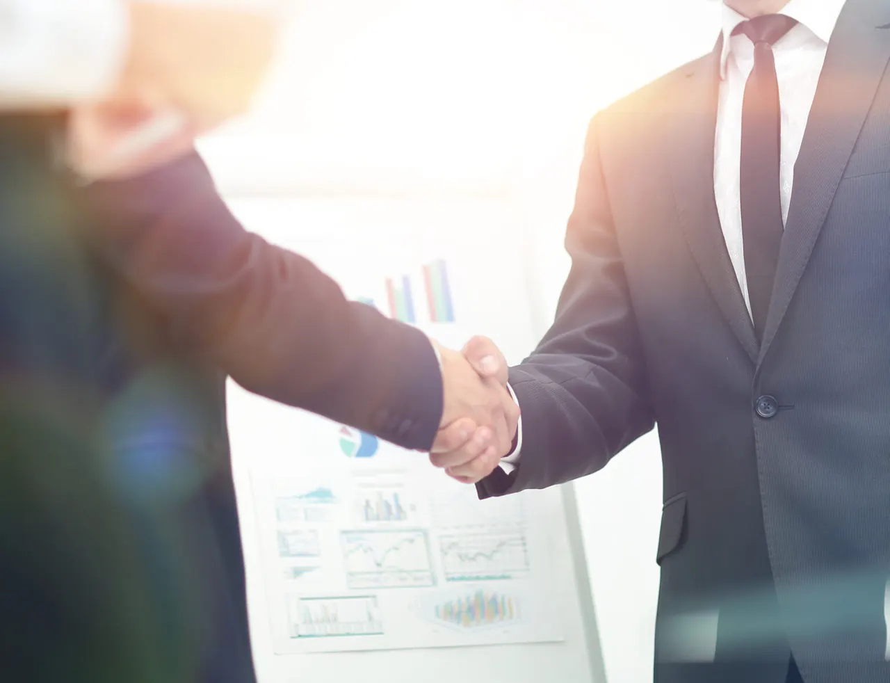 Two professionals shaking hands in front of business charts